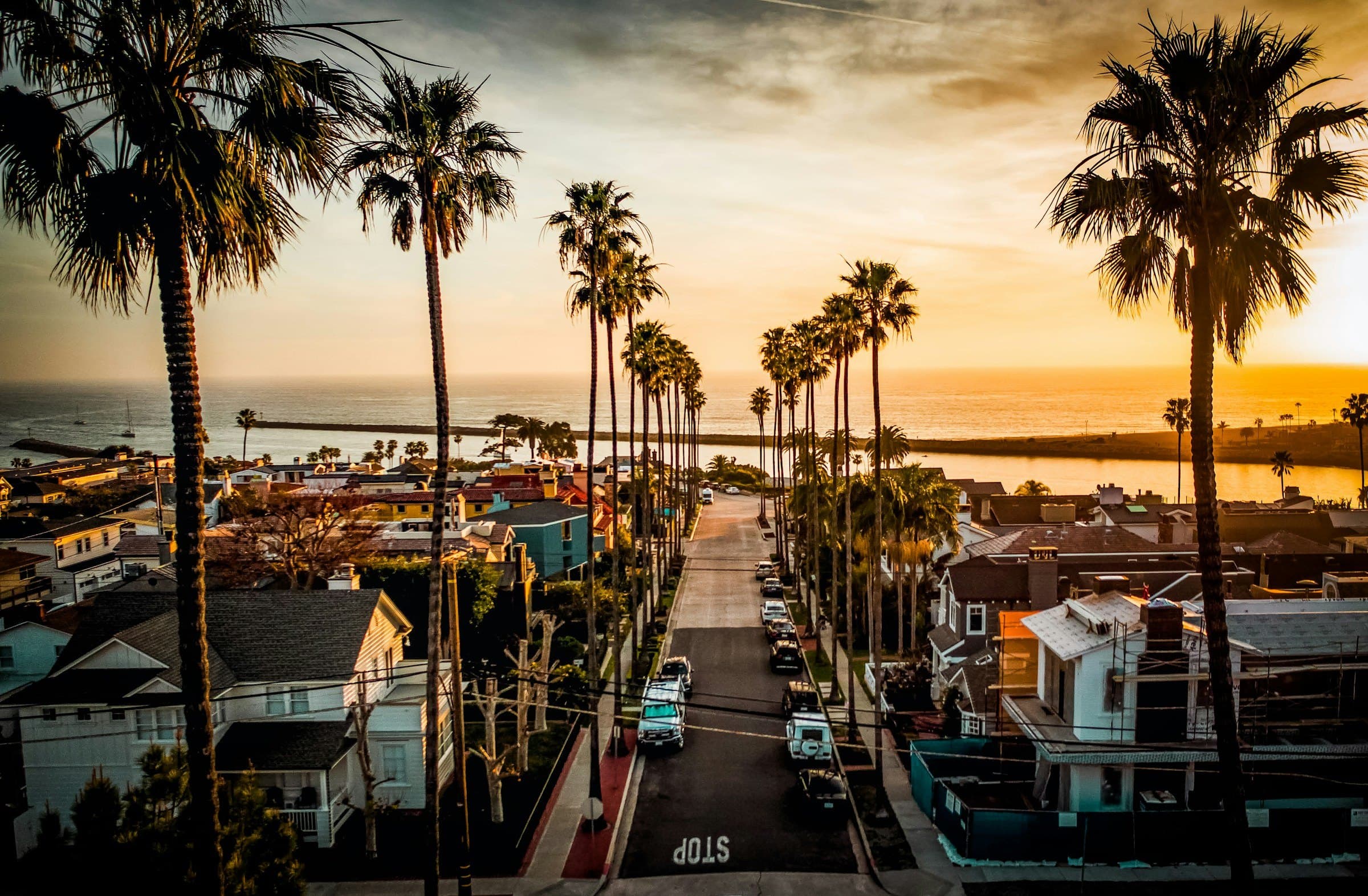 A residential street in Corona del Mar at golden hour, with Newport Harbor beyond